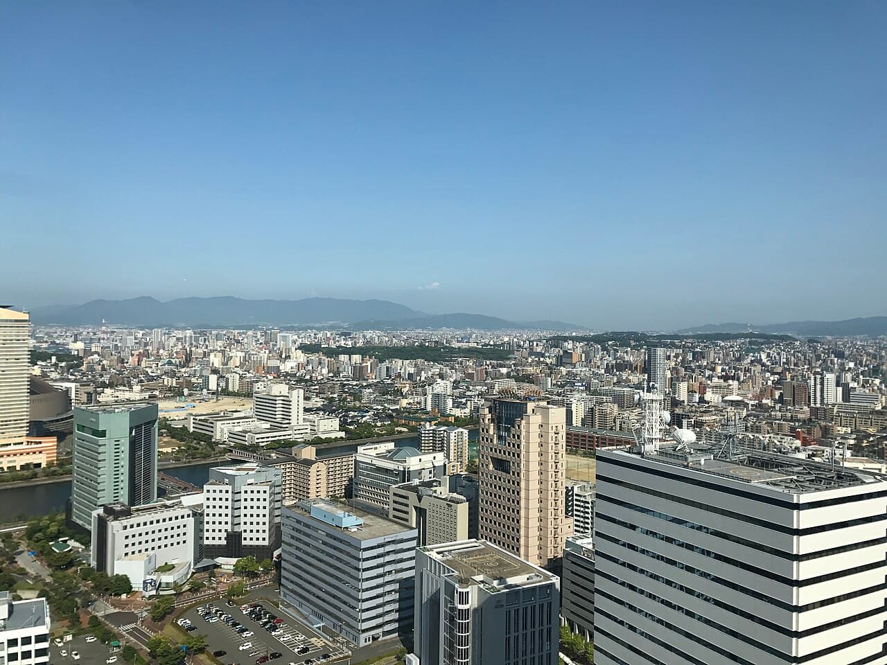 Fukuoka seen from Fukuoka Tower in Momochi: office blocks in the foreground, then dense mid-rise buildings stretching inland to the mountains